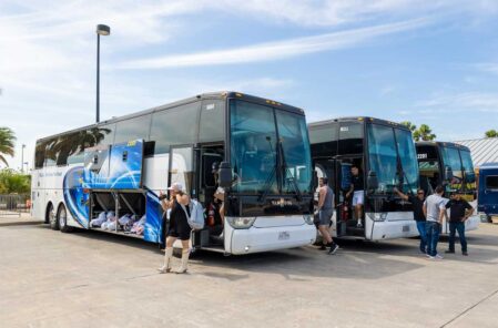 A diverse group of people standing together in front of a bus, smiling and engaging with one another.