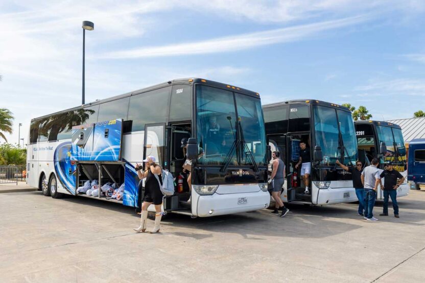 How to Plan a Multi-Day School Sports Trip A diverse group of people standing together in front of a bus, smiling and engaging with one another.