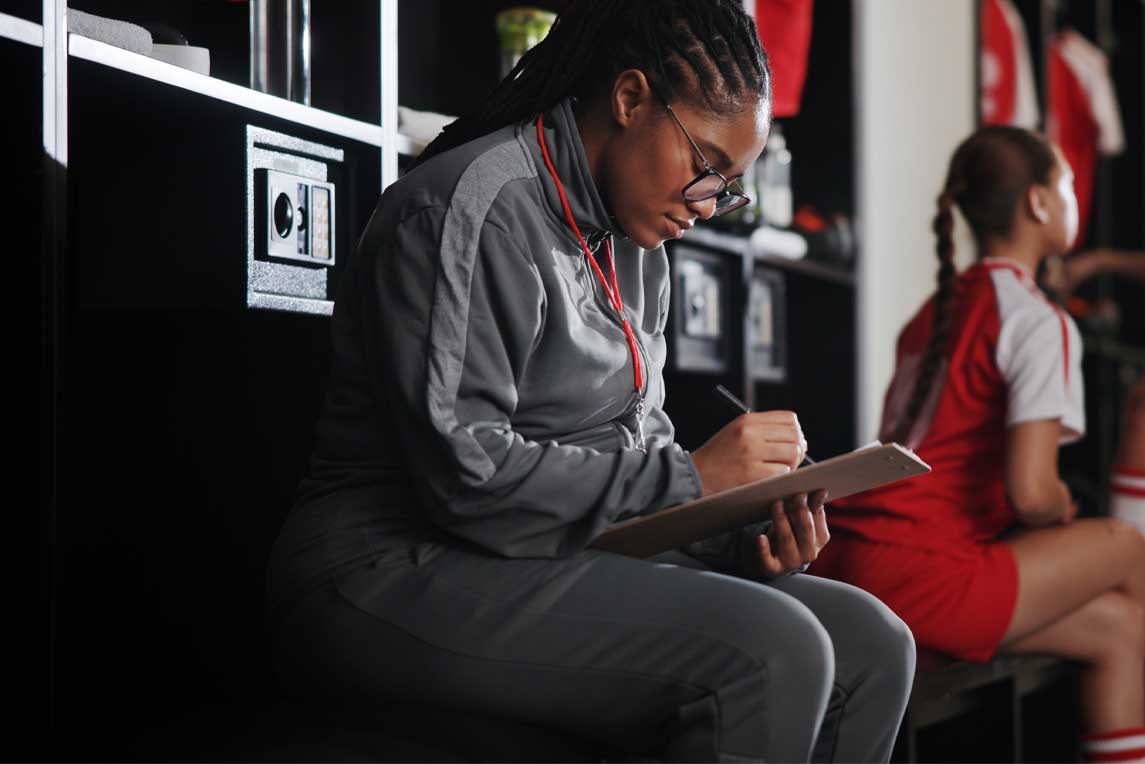 Woman, soccer coach and writing with clipboard for checklist, game plan or attendance list in locker room. Female person, manager or coordinator with notes for match, sport or player registration